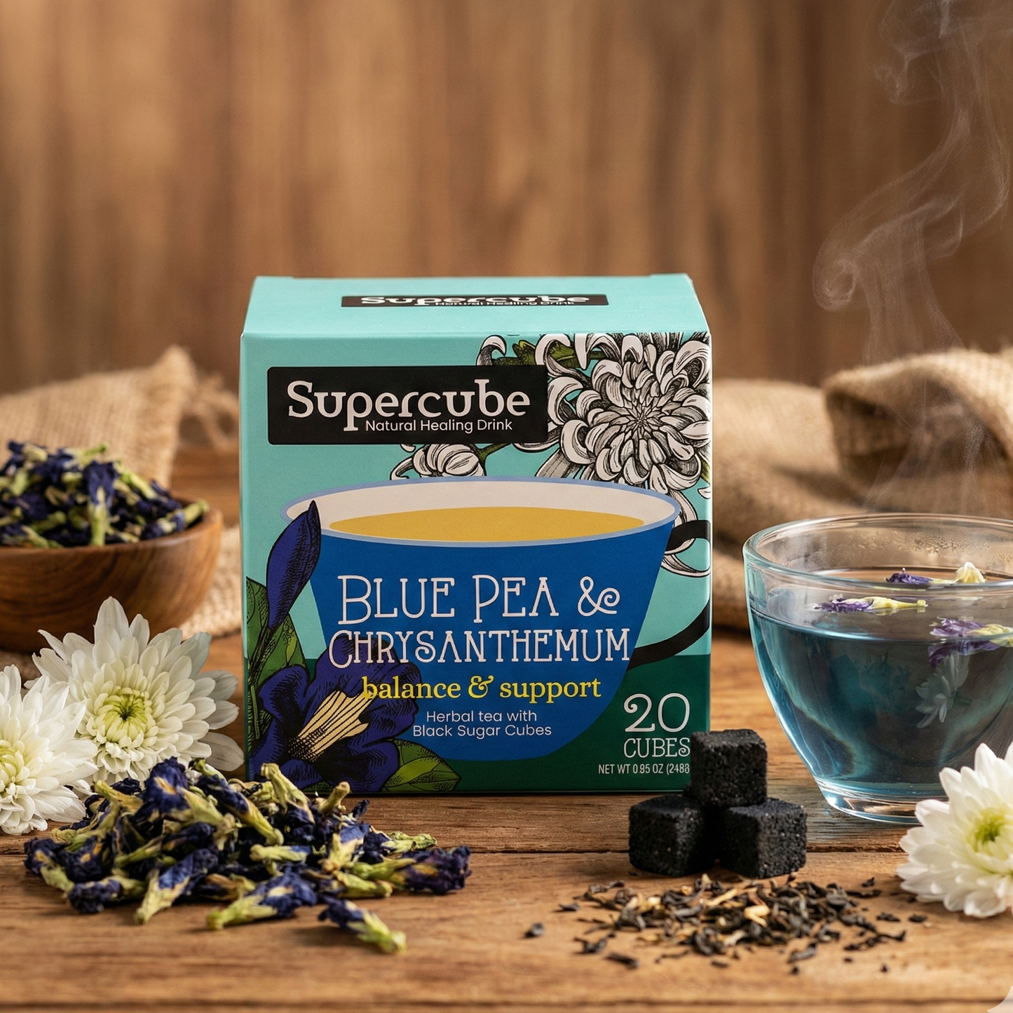 Supercube Blue Pea & Chrysanthemum tea packaging on a wooden surface with tea leaves and flowers.